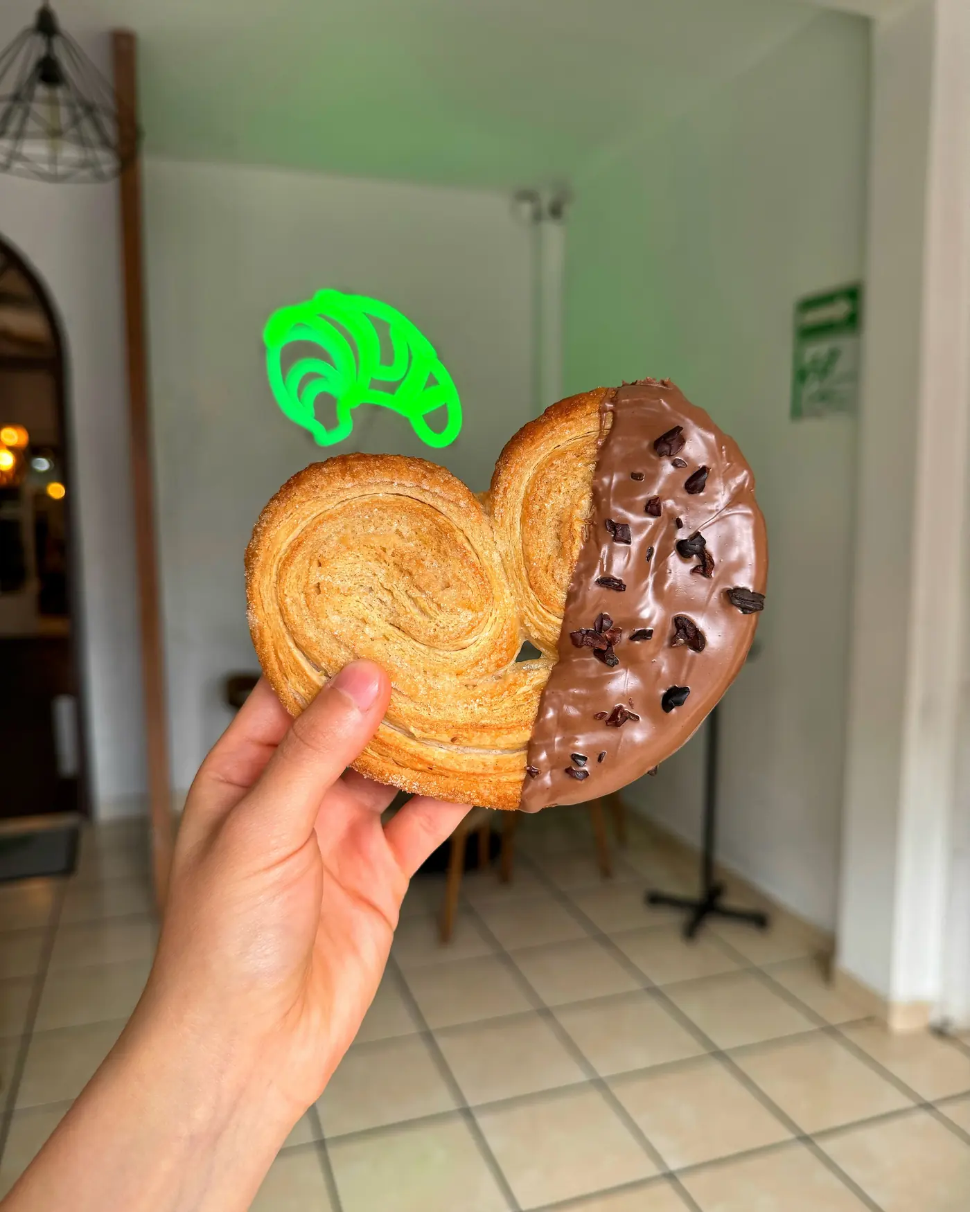 Orejita de hojaldre bañada de chocolate frente al letrero de neón